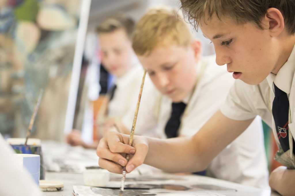 Three male Leigh Academy students painting together in an Art class.