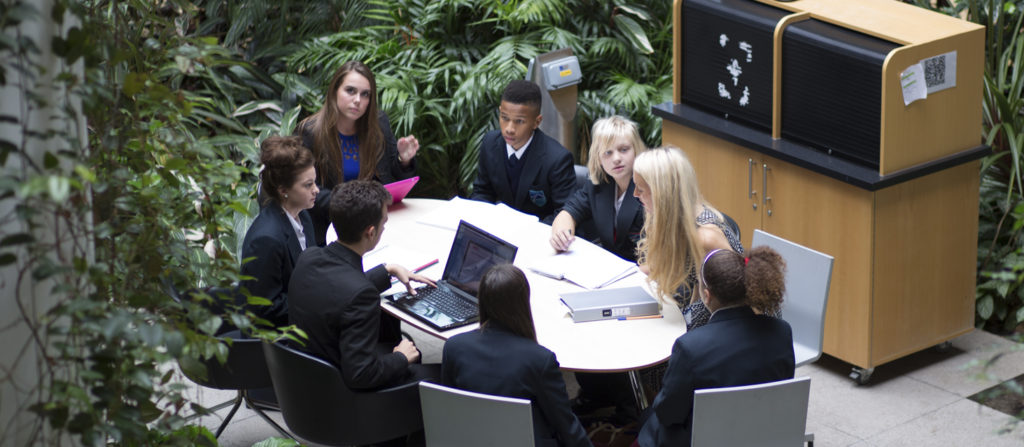 Small group of Leigh Academy students gathered around an oval-shaped table, speaking with members of staff.