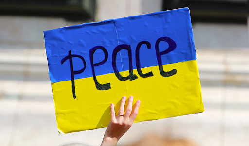 A cardboard placard is seen held up with the blue and yellow colours of the Ukraine flag with the word 'Peace' written across it.