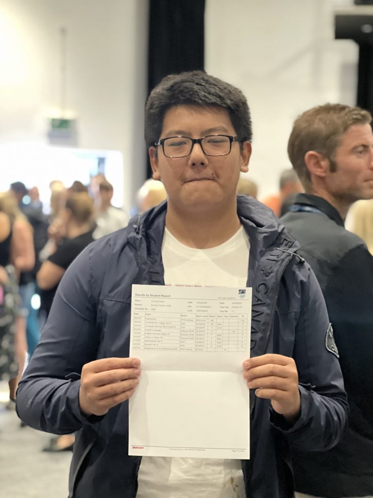 Year 11 student, Annukul G, is shown holding up his results sheet for the camera and smiling on GCSE Results Day 2022.