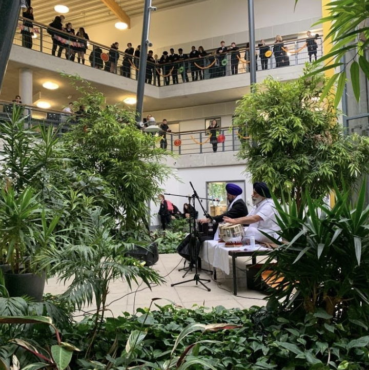 Photo showing two men performing traditional Asian music in an open atrium area of The Leigh Academy building. Students are seen listening from the surrounding balconies.