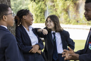 A group of four students are seen laughing and conversing with one another outdoors, whilst wearing their academy uniform.