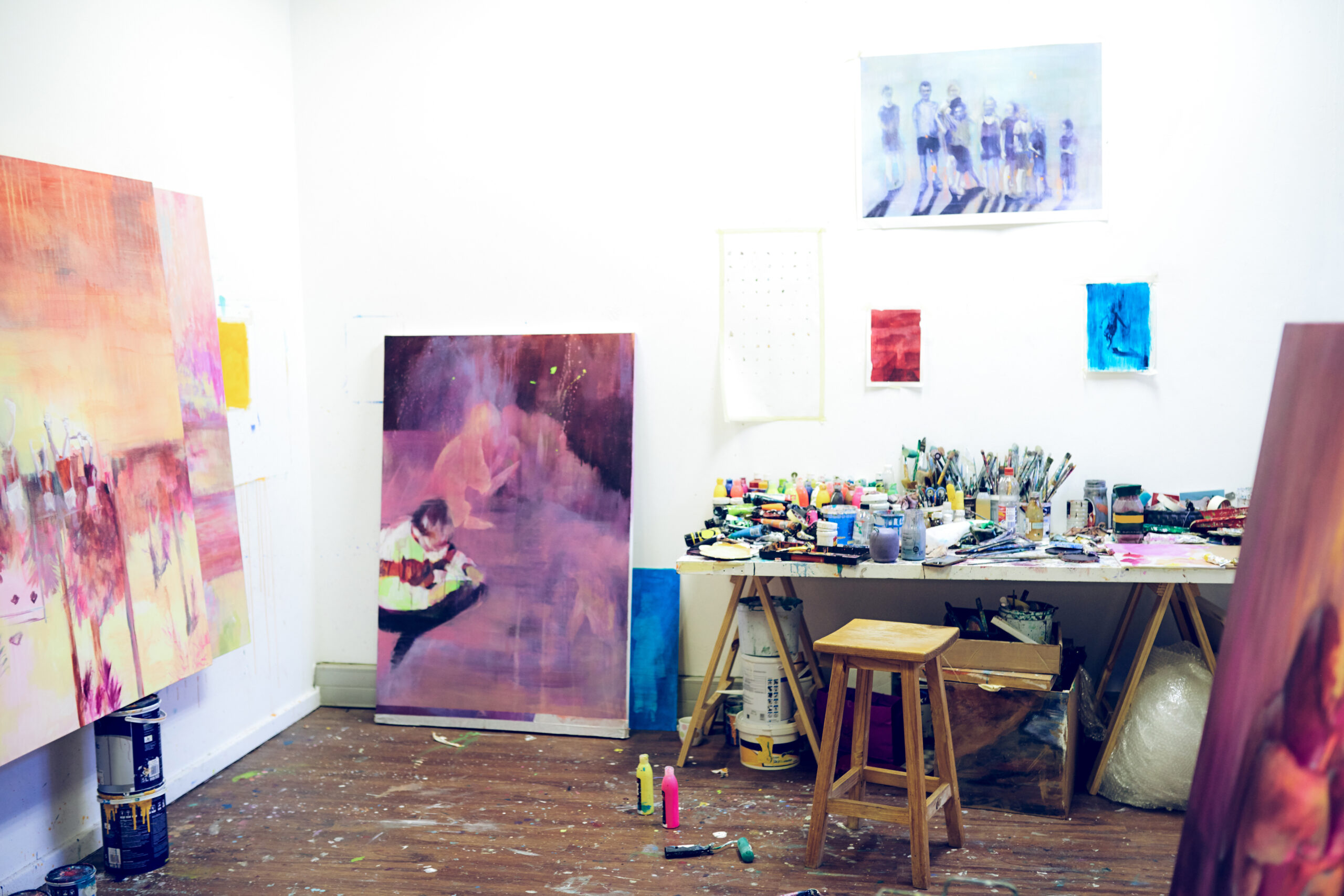 A photo of an artist's studio with canvases seen on stands and painting supplies situated on a table to the side.